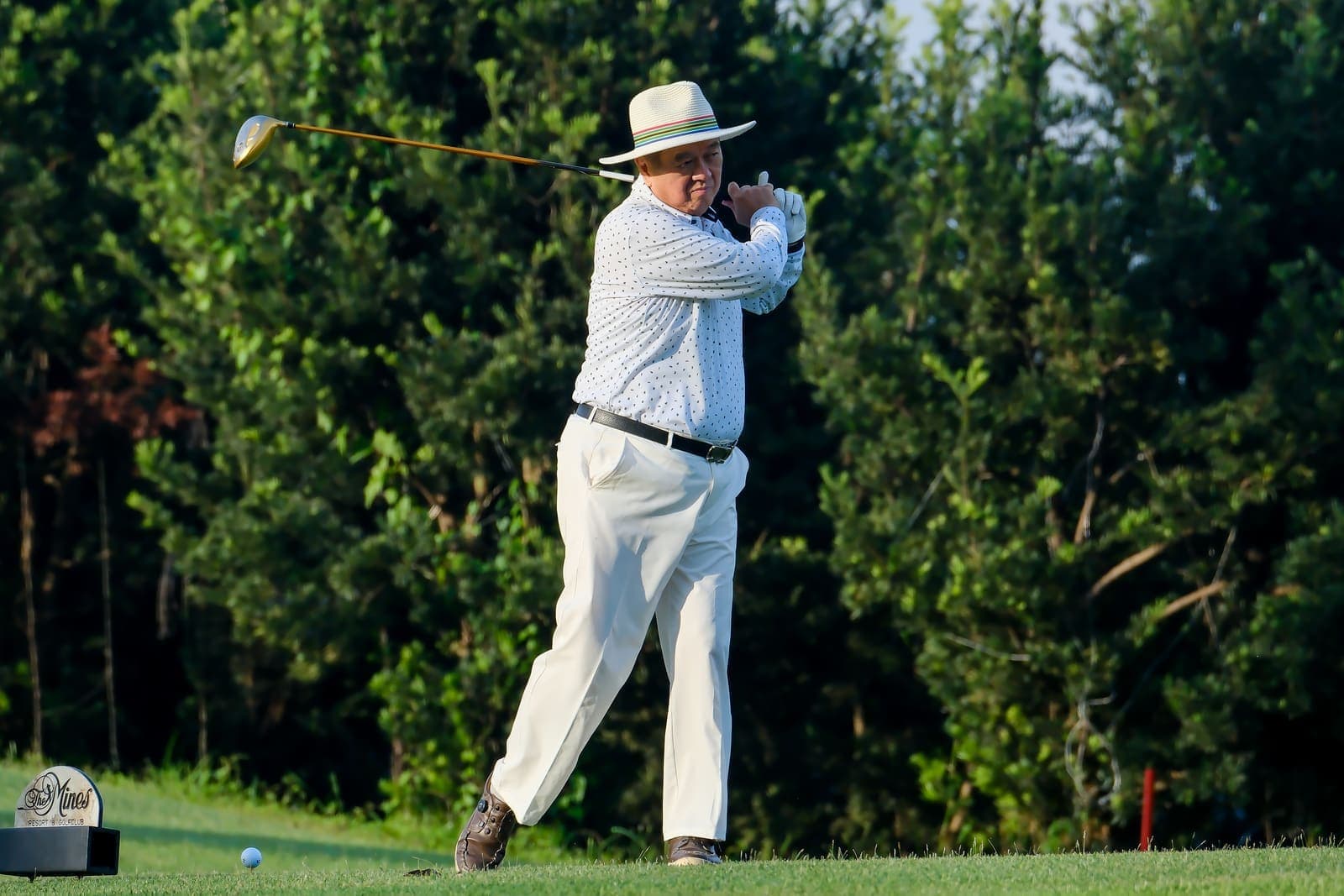 A club member teeing off on the course, The Mines Resort & Golf Club signage visible on the tee marker