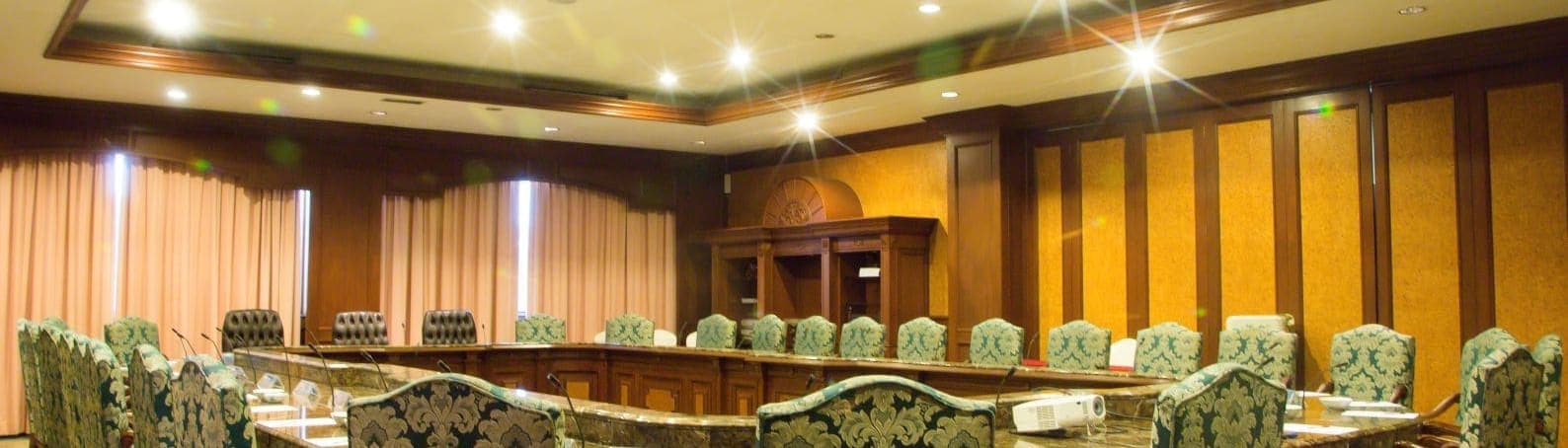 A boardroom with a U-shaped conference table, patterned chairs and microphones