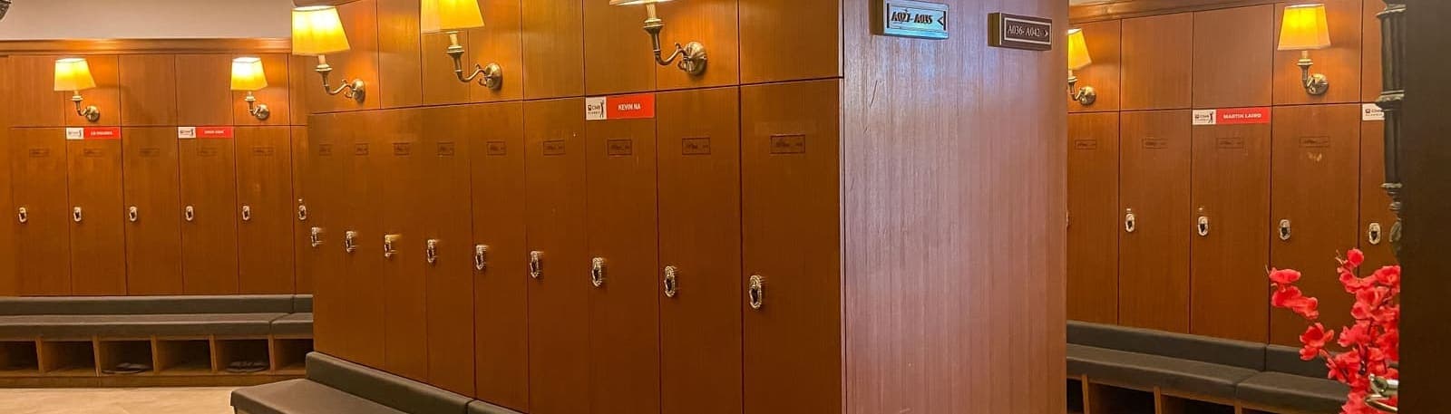 A row of wood locker units with brass wall lamps and members' name plates