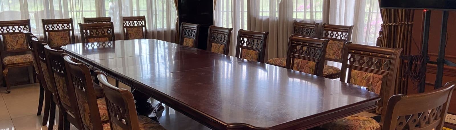 A long meeting table set for ten with upholstered chairs beneath sheer curtained windows