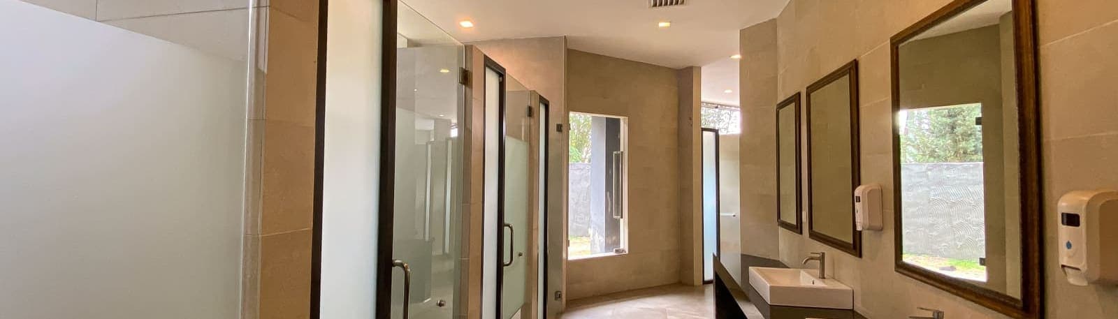 A row of glass-partitioned shower stalls beside a vanity counter with mirrors