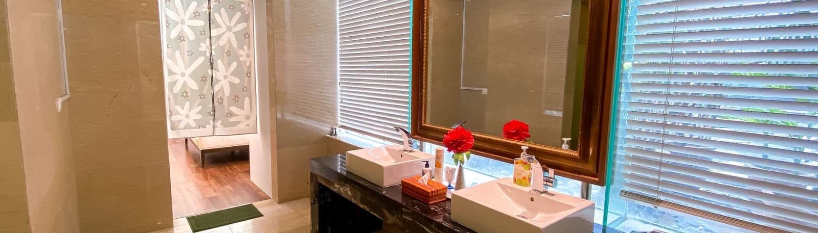 A vanity counter with dual basins, ornate mirrors and a floral arrangement