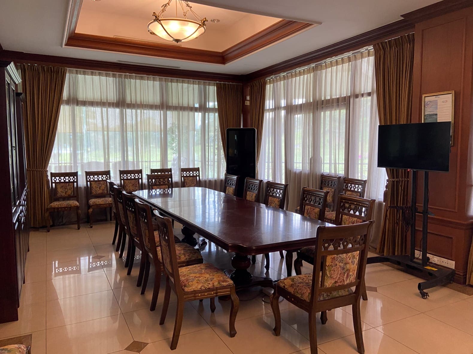 A private meeting room set for twelve, with a long wood table, upholstered chairs and a wall-mounted display screen