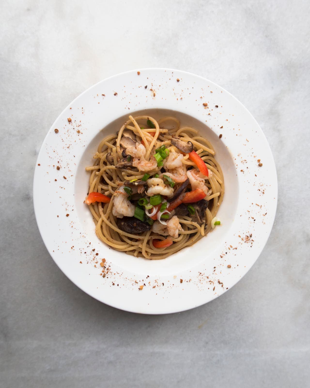 A plated seafood spaghetti dish with prawns, mushrooms and peppers, dusted with cracked pepper