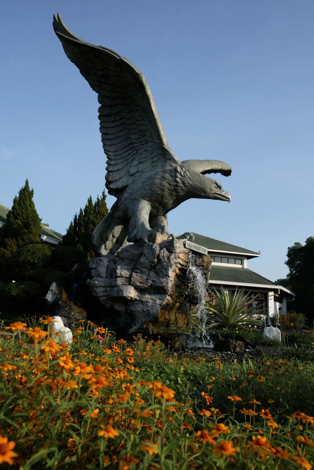 The club's eagle statue perched on a rock waterfall feature, framed by marigolds in bloom