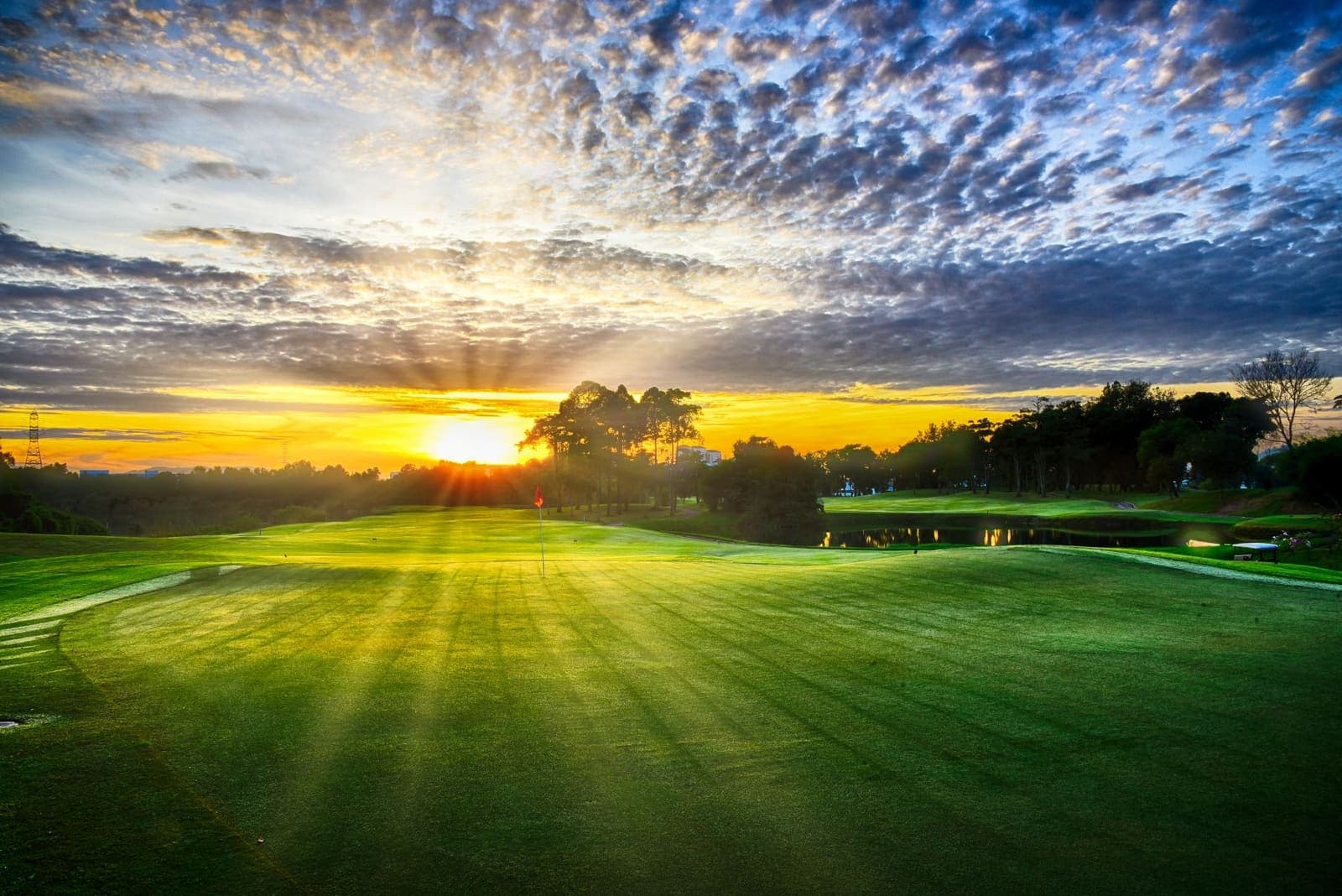 Sunrise over a green and flagstick, sun rays breaking through the tree line