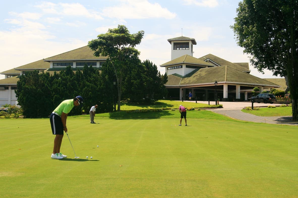 Golfers practicing on the putting green in front of the clubhouse entrance