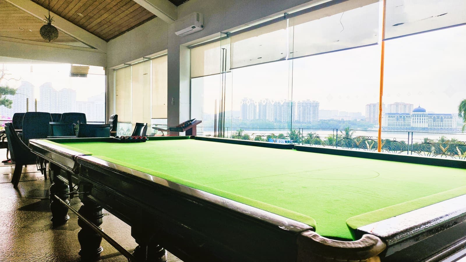 A billiards table beside floor-to-ceiling windows overlooking the lake and city skyline, with a dining table beyond