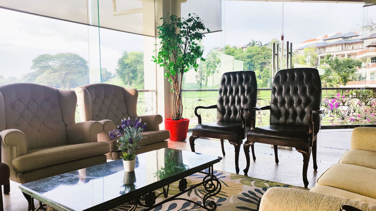 A glass-walled lounge with armchairs and a potted plant overlooking a landscaped balcony and the resort's villas