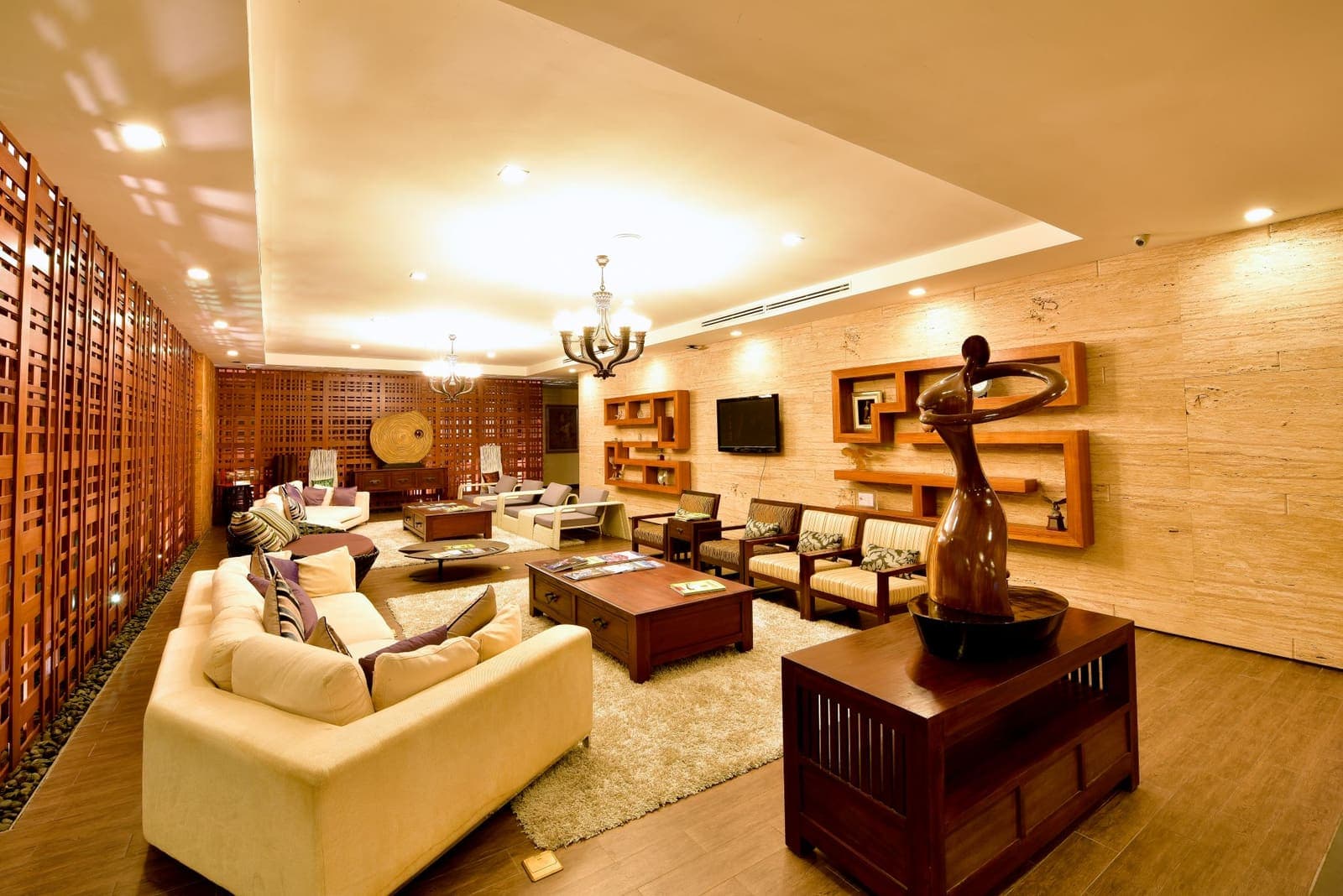 A lounge seating area with cream sofas, a carved wood sculpture and a wood lattice-screen wall panel